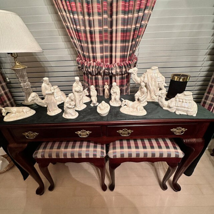 Velvet table runner with decorative nativity scene on a wooden side table with plaid benches and curtains in the background.