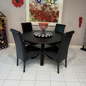 Black round dining table with four chairs in a room with decorative elements.