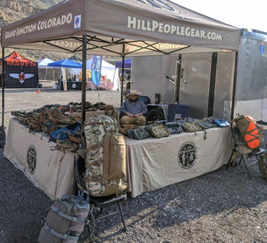 Printed table linens with black logo with military-style bags on top for Hill People Gear