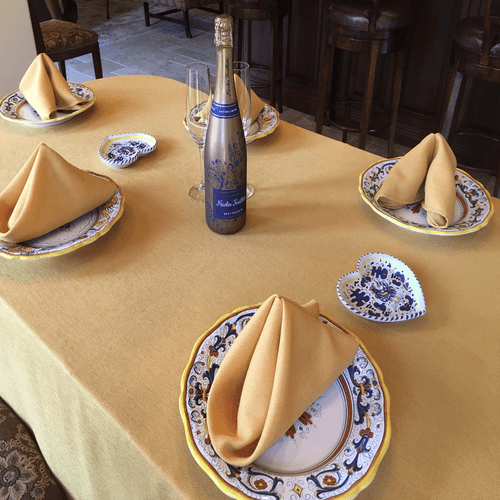 Our Gold colored Havana napkins on plates on an intimate home dining table with a bottle of champagne