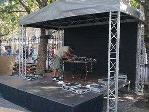 Black stage skirt on small stage with DJ equipment being set up under tent with trussing