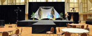Large stage set up with black flat wrap stage skirt around the entire stage with lights, trussing & sails