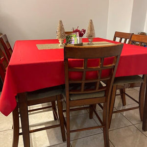 Square table with holiday red tablecloth on a home dinner table with small Holiday ornaments