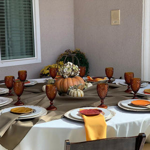Round Table with white tablecloth, green runner, and gold napkins in a backyard