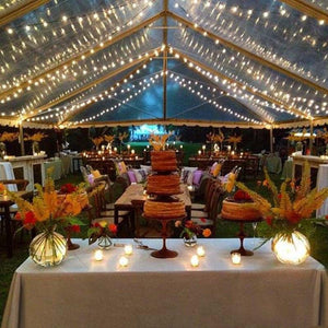 Tan table linens on an outdoor event's main table under a tent with cake and candles