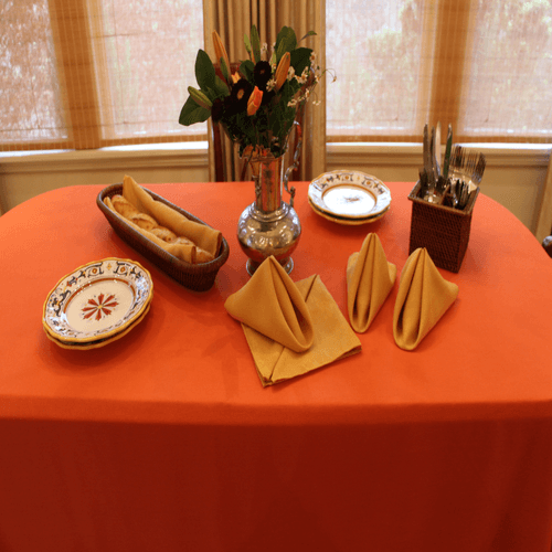 Rectangular orange formal linens on a small serving station table with bread and flowers on it