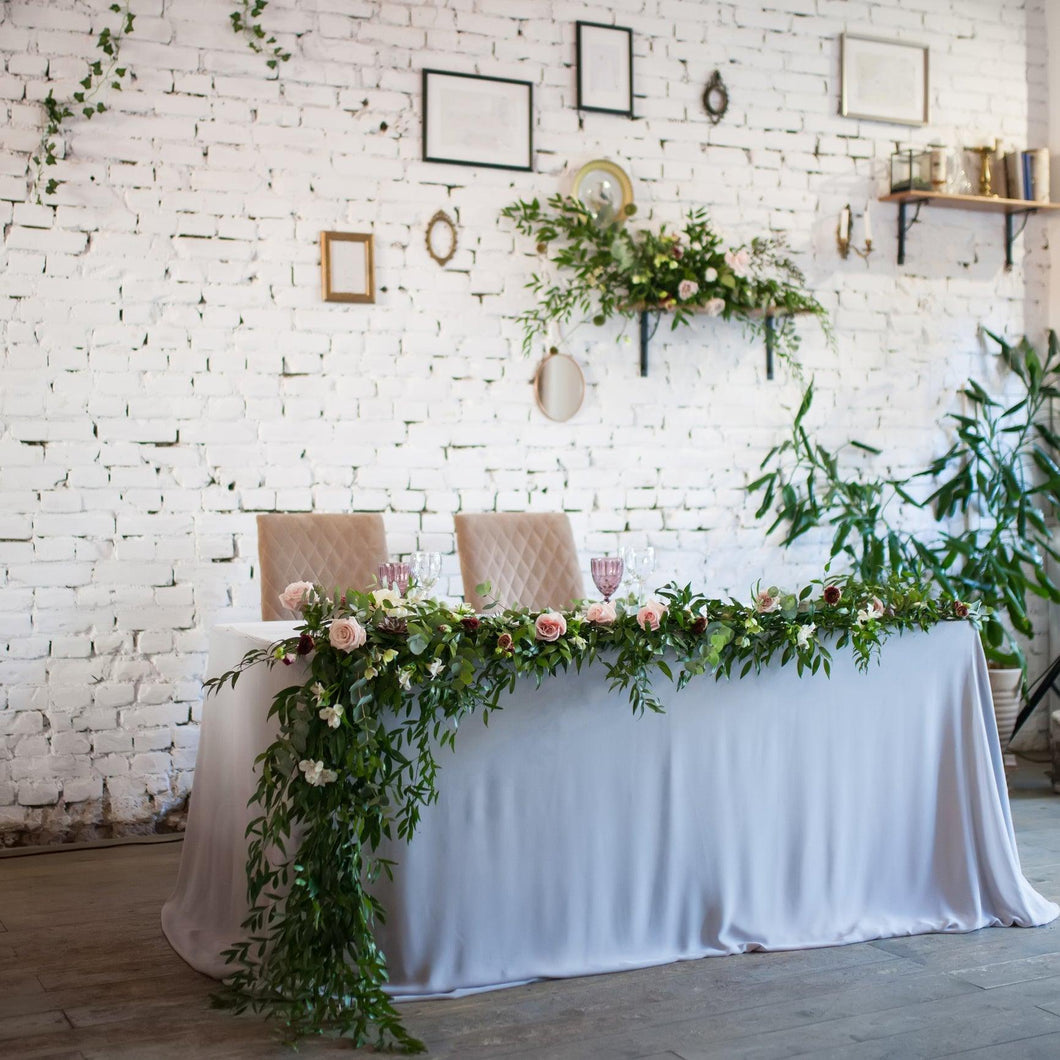 White wedding linens on the head table at a banquet reception with flower decore and glasses