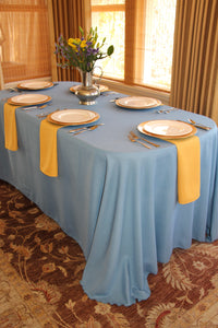 Light blue colored table linens with Golden napkins under place settings for 6 by a window