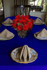 A royal blue tablecloth on an oval table with natural colored napkins, plates, and roses
