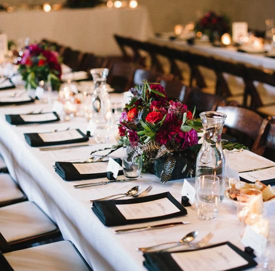 White Table cloth on a long table in a celebratory dining environment with Black Napkins