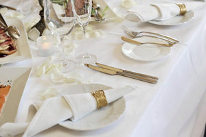 White tablecloth on a table at a banquet style reception with candles, glasses, and cutlery