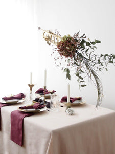 White tablecloth on table in a photoshoot setting with burgundy napkins, plates, and candles