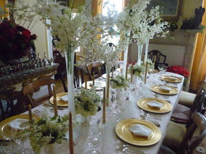 Fine linens on a table in a fancy home dinner setting with gold plates and large flower centerpieces