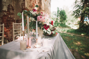 White formal wedding linens on an outdoor table with candles, plates, and flowers