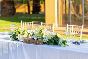 Elegant linens on an outdoor wedding head table with white roses and a wooden