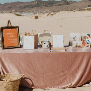 Rose color velvet linens on a wedding signing table on the beach with photo frames and book