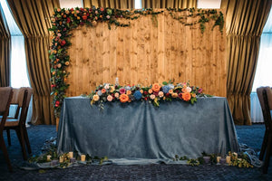 Wedding linens on the lead table at a wedding reception with Flowers in front of a wooden backdrop