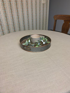 Formal table linens on a round table in a home setting with a metal tray at the center