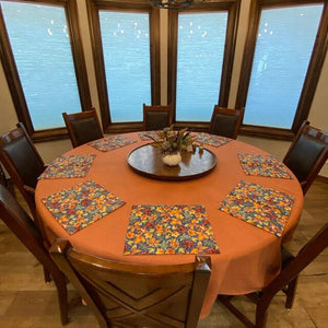 a round tangerine colored tablecloth on a table with seating for 8 with floral placemats
