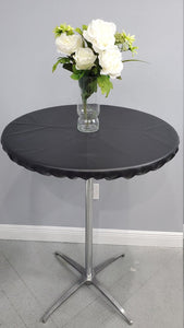 A black, round fitted vinyl tablecloth with vase of white roses