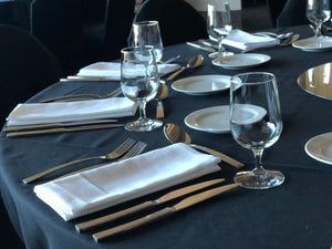 Round Table close up with blue linens and white napkins on plates with drinking glasses and cutlery