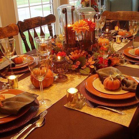 Brick colored table linens with a gold runner and matching placemats and Thanksgiving decorations