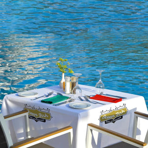 Square custom-printed white tablecloth with restaurant logo set up for lunch by the water