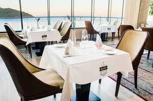 Fine white linens with full-color print on various tables at a  High end restaurant by a big window