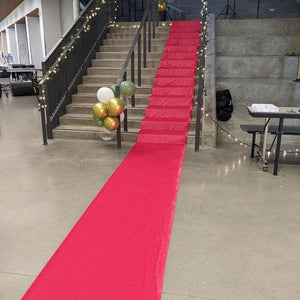 A red wedding aisle runner set up down a stairway and across the room with balloons on the railing