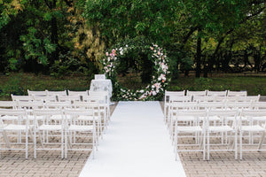 Outdoor wedding aisle runner with white folding chairs on each side 
