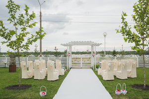 White aisle runner at an outdoor wedding reception with ivory colored chair covers 